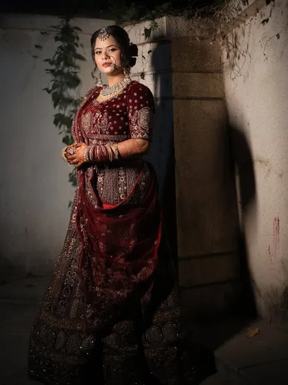 A full-length shot in a moody setting, highlighting the richness of the bride's velvet lehenga and her confident pose.