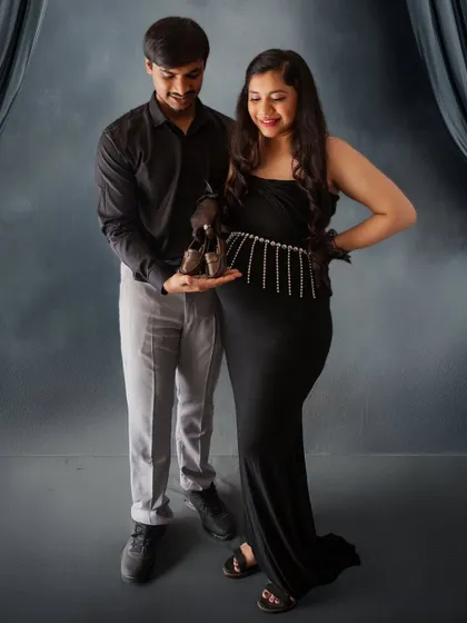 A classic and sweet announcement photo. The couple holds up a pair of tiny baby shoes, a timeless symbol of the new life they are waiting for.