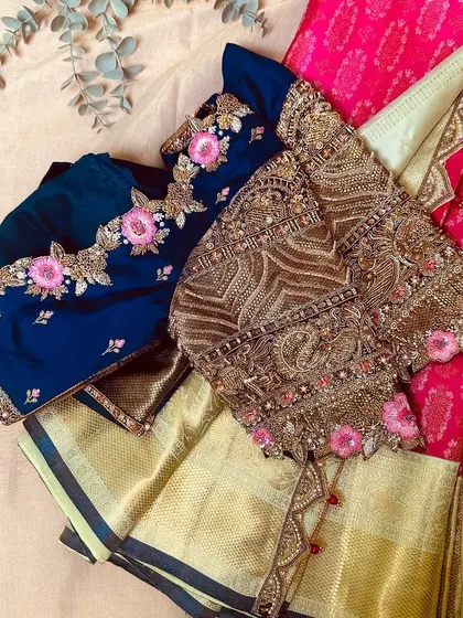 A flat lay of two stunning blouses, one in navy with pink florals and another with heavy gold embroidery.
