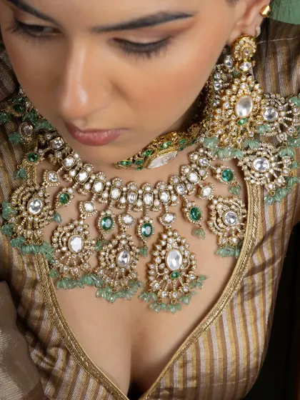 A detailed overhead shot of a layered Kundan choker with emerald accents. You can see the precision of the stone setting and the delicate beadwork that defines our craftsmanship.