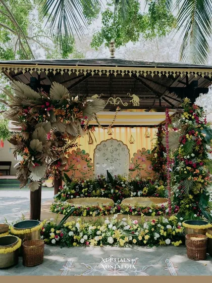 A stunning Haldi mandap featuring a unique blend of dried palm leaves and fresh, colorful flowers, creating a rustic yet vibrant aesthetic.