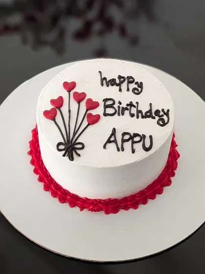 A simple yet heartfelt birthday bento cake. The clean white buttercream is decorated with a hand-piped bouquet of heart balloons and a red piped border, wishing "Appu" a happy birthday.