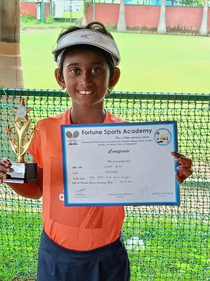 A smiling Girls U10 winner proudly displays her trophy and certificate from an All India Tennis Association tournament we hosted. Our events for younger age groups focus on positive reinforcement and building confidence.