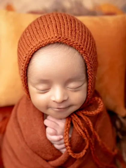 A sweet, smiling newborn in our autumn-themed setup. The warm colors and that happy expression are a perfect match.