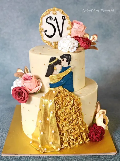 This two-tier cake was designed for an anniversary, featuring a hand-painted couple in traditional Indian attire. The intricate golden ruffled skirt and monogram plaque make it a deeply personal and celebratory centerpiece.