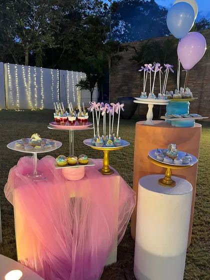 A dessert table at a unicorn-themed party. The setup includes various treats on stands of different heights, set against a backdrop of pink tulle and balloons, creating a sweet and magical display.