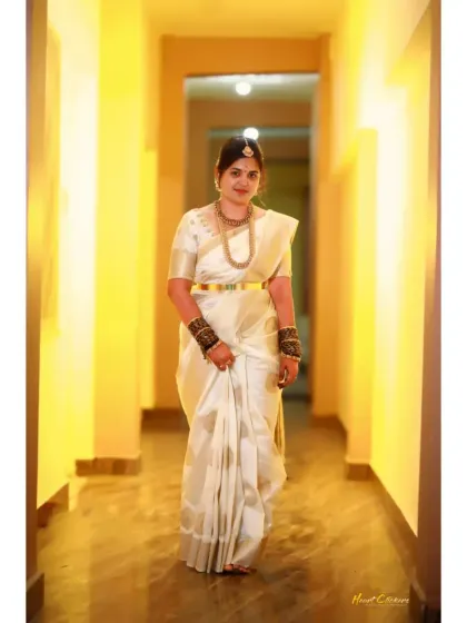 A full-length portrait of the bride in a beautiful white saree, walking down a warmly lit hallway.