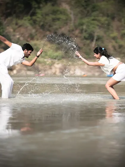 A fun, candid moment of a couple splashing each other in a river, showcasing their playful connection during their pre-wedding shoot.