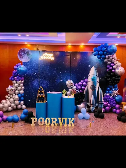 An out-of-this-world space and rocket theme for Poorvik's 6th birthday. The decor includes a galaxy backdrop, a large rocket prop, and planet-like balloons in silver, blue, and purple.