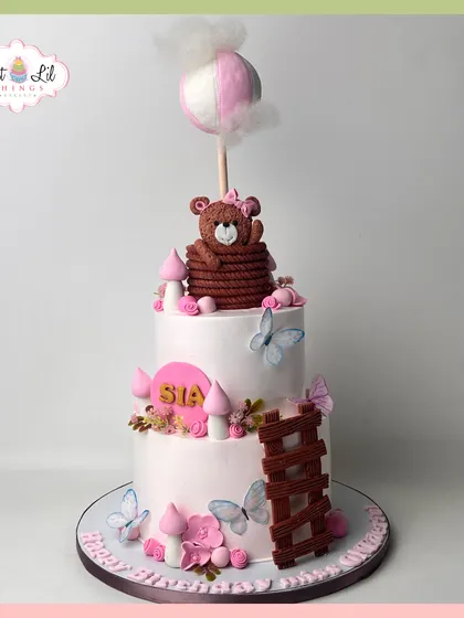 A fairytale cake for Sia's birthday, featuring a teddy bear in a hot air balloon, delicate butterflies, and a whimsical ladder.