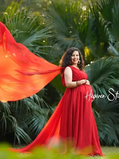 The flowing red fabric of her gown catches the light beautifully in this outdoor portrait, creating a sense of movement and life.