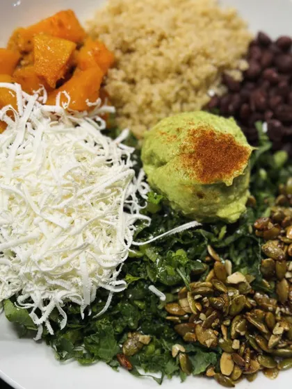 A vibrant and nutritious Buddha bowl with quinoa, roasted butternut squash, black beans, kale, shredded cheese, and guacamole.