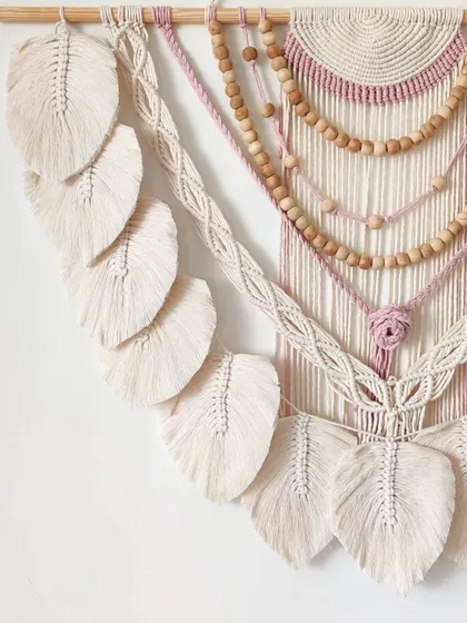 A side view of the mauve and cream wall hanging, highlighting the layers of beads and knots.