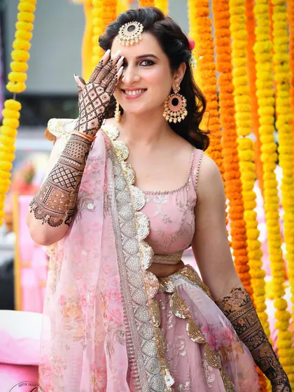 A beautiful portrait of a bride during her mehndi ceremony. Her joyful smile and the vibrant marigold background create a picture of pure happiness and celebration.