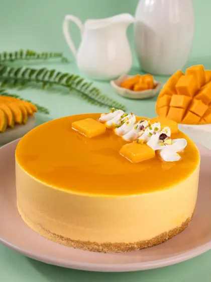 A smooth and glossy mango cheesecake, styled with fresh mango slices against a pastel green background.