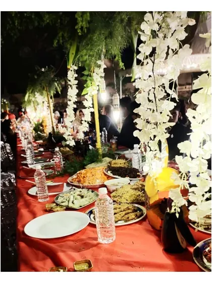 An intimate and beautifully decorated outdoor wedding setup. The long table is adorned with hanging white flowers, creating a magical atmosphere for the feast.