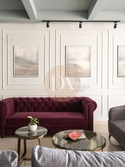 A living room from one of our featured projects, with a bold burgundy Chesterfield sofa set against a wall with classic molding. The mix of grey and burgundy upholstery creates a sophisticated and layered look.