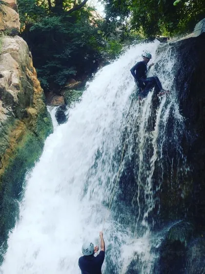 A student practices their rappelling form on the waterfall, with an instructor providing belay support from below.