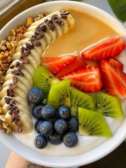 A vibrant and healthy smoothie bowl, topped with granola, fresh banana, strawberries, kiwi, and blueberries. A perfect option for a health-focused event.