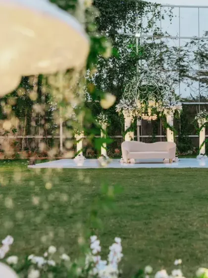 A wide view of a garden reception setup, featuring a beautiful white gazebo and elegant seating arrangements surrounded by lush greenery.