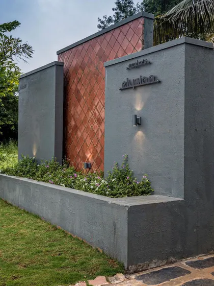 A close-up of the entrance detail, showcasing the material palette of textured concrete and copper-toned tiles, complemented by soft landscape lighting.