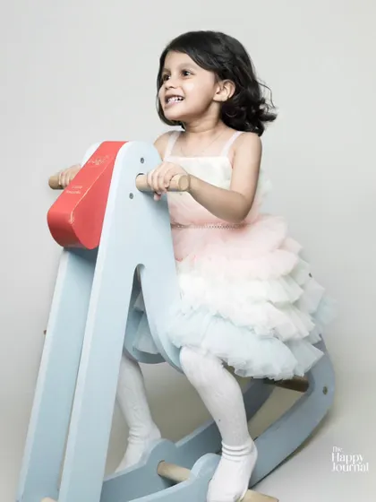 A little girl in a pastel tutu dress enjoys a ride on a rocking horse. A classic and joyful childhood portrait.