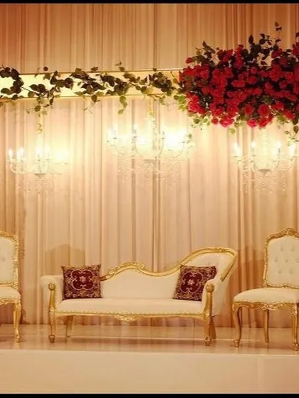 This is an example of a classic and elegant stage design that feels both grand and intimate. I used a simple frame draped with red roses and green vines, with crystal chandeliers hanging above a traditional white and gold chaise lounge for a timeless look.