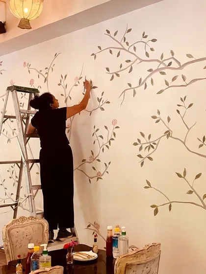 Me on a ladder, carefully painting the delicate branches and leaves for the Cafe Wink mural. This vintage style requires a soft touch and attention to detail.
