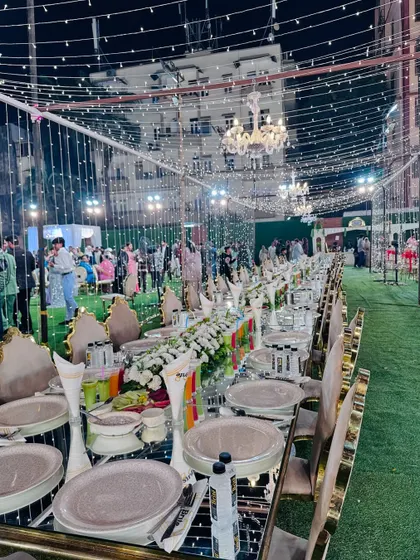 A breathtaking view of a long, formal dining arrangement under a canopy of fairy lights and chandeliers.