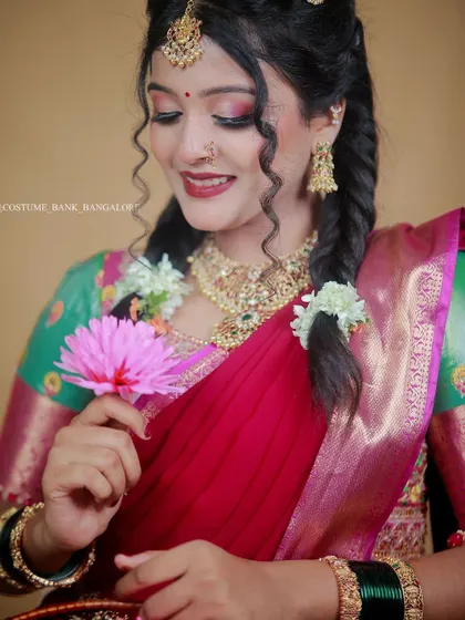 A close-up portrait of a model in a beautiful red and green half-saree, adorned with traditional jewelry and flowers in her hair.