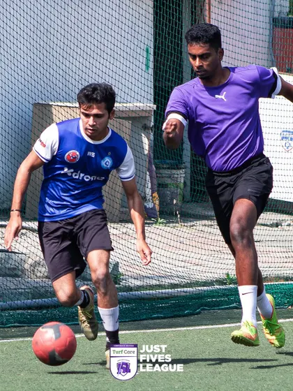 A player skillfully dribbles the ball while being pursued by a defender. The fast-paced action of the Just Fives League keeps everyone engaged.