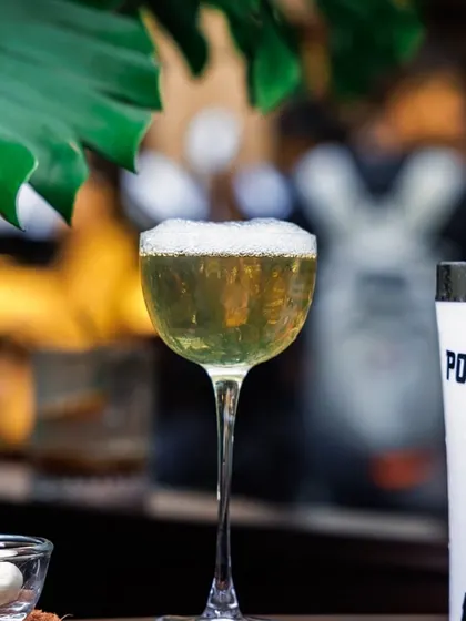 The final presentation of our "Pour Toujours" cocktail, complete with a delicate foam top and served alongside its shaker. This showcases our dedication to the complete craft cocktail experience.