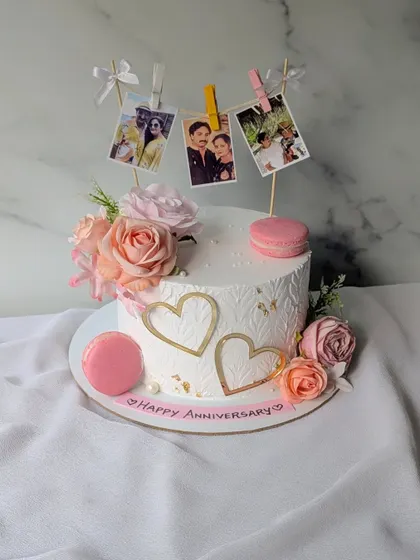 A sweet anniversary cake decorated with a clothesline of edible photos of the couple, surrounded by fresh flowers and macarons.