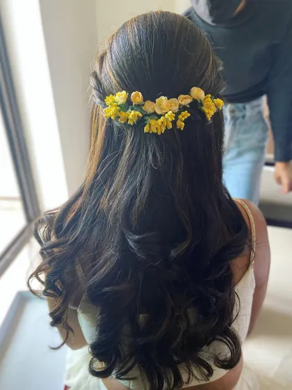 A beautiful half-up hairstyle for a Haldi ceremony, adorned with a crown of fresh yellow flowers.