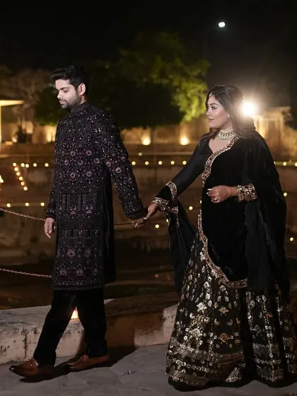 The couple, dressed in elegant black, walks hand-in-hand through the candle-lit ambiance of their Retro Sufi sangeet.