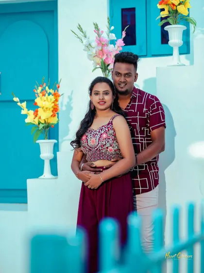A classic portrait of a couple in a Santorini-style setting. The vibrant flowers and colorful architecture create a cheerful and romantic backdrop.