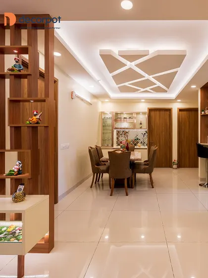 This spacious living and dining area is perfect for a large family. We used a wooden partition to create a subtle separation while maintaining an open feel, complemented by a geometric false ceiling design.
