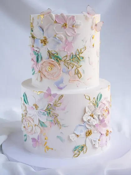 A stunning two-tiered cake featuring pastel, hand-painted floral details with gold accents. This technique, known as palette knife painting, creates a beautiful, artistic texture.