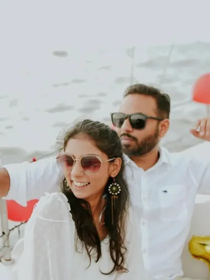 A cool, candid shot of a couple enjoying their pre-wedding shoot on a sailboat, with sunglasses and red balloons adding a fun, celebratory touch.
