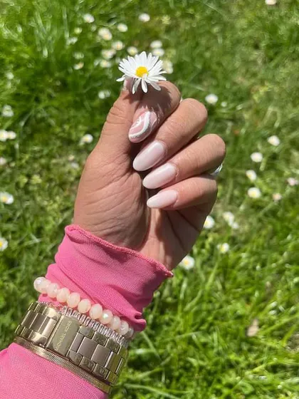 A happy client showing off her fresh manicure. This simple yet beautiful design features a soft, milky pink base with a delicate white swirl accent on one nail, perfect for everyday elegance.