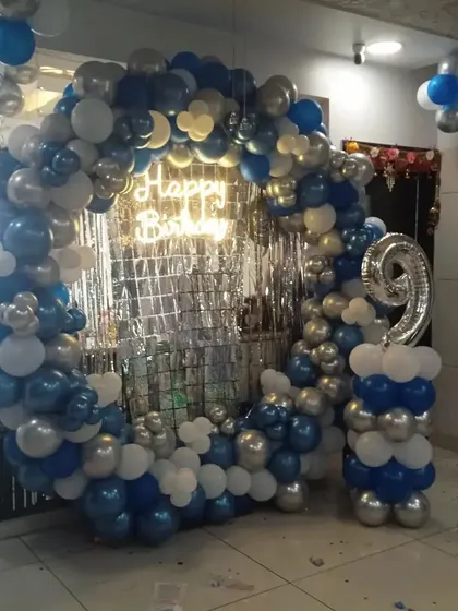 A blue and silver balloon ring with a silver tinsel backdrop, set up in a spacious room or small hall.