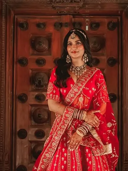A regal portrait of the bride in a classic red saree. Her direct gaze and confident posture against a grand architectural backdrop create a powerful image.
