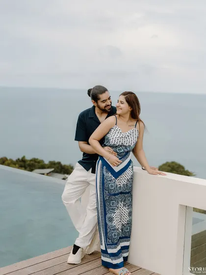 A serene portrait of a couple on a balcony overlooking an infinity pool and the ocean in Thailand.