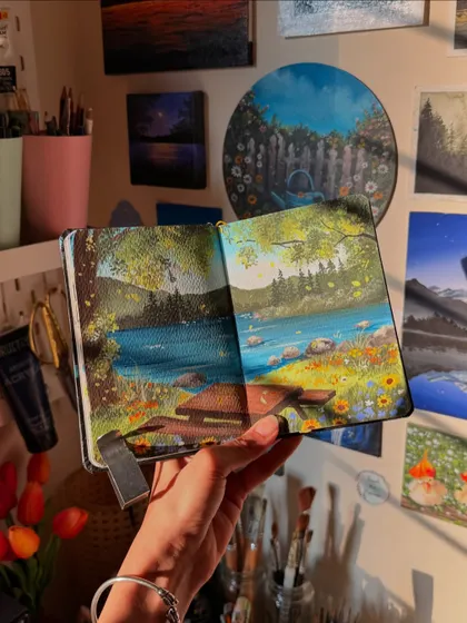 Holding my picnic painting sketchbook in front of my art wall. It’s one of my favorite cozy scenes that I have created.