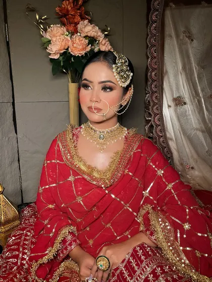 A bride seated in a classic red suit-style lehenga, showing the intricate gold grid pattern.