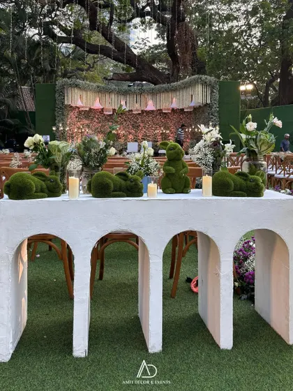 A whimsical decor detail featuring moss bunnies on an arched white table, adding a touch of playful charm to an elegant outdoor wedding setup.