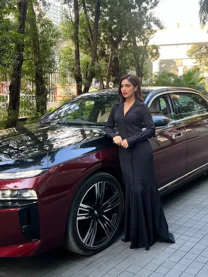 Here is the complete look for Bhumi Pednekar at the BMW India event. Standing next to the car, the long, flowing silhouette of the black Qua Clothing gown complements the sleek lines of the vehicle, creating a cohesive image of luxury.