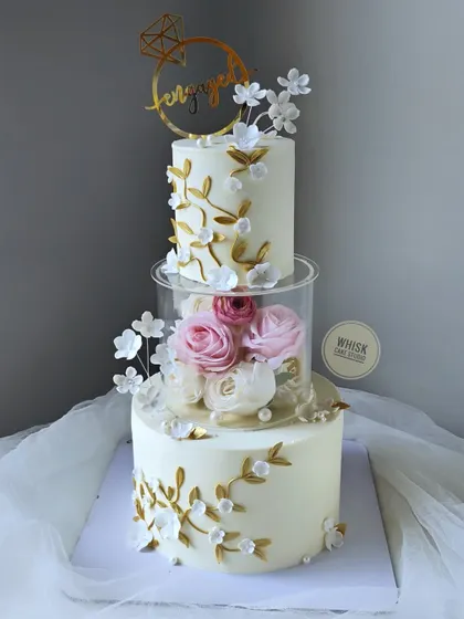 A classic and elegant engagement cake. This design features two real cake tiers separated by a clear acrylic tier filled with fresh flowers, combining modern and traditional elements beautifully.