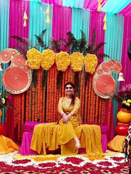 A happy bride posing against a vibrant Haldi backdrop. The combination of marigolds, paisley motifs, and colorful drapes creates a joyful and photogenic setting.