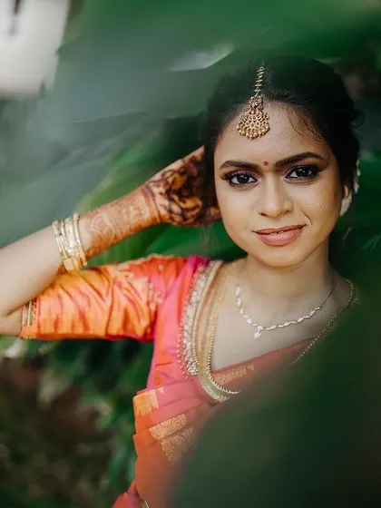 A close-up portrait of a South Indian bride, framed by leaves, highlighting her beautiful features.